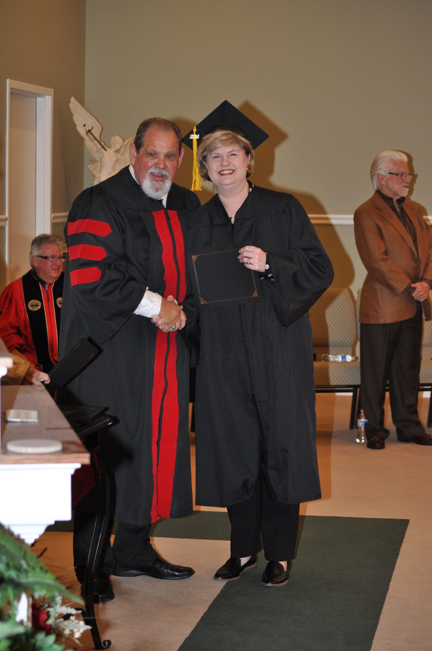 Person in graduation gown shaking hands with another person during a ceremony.