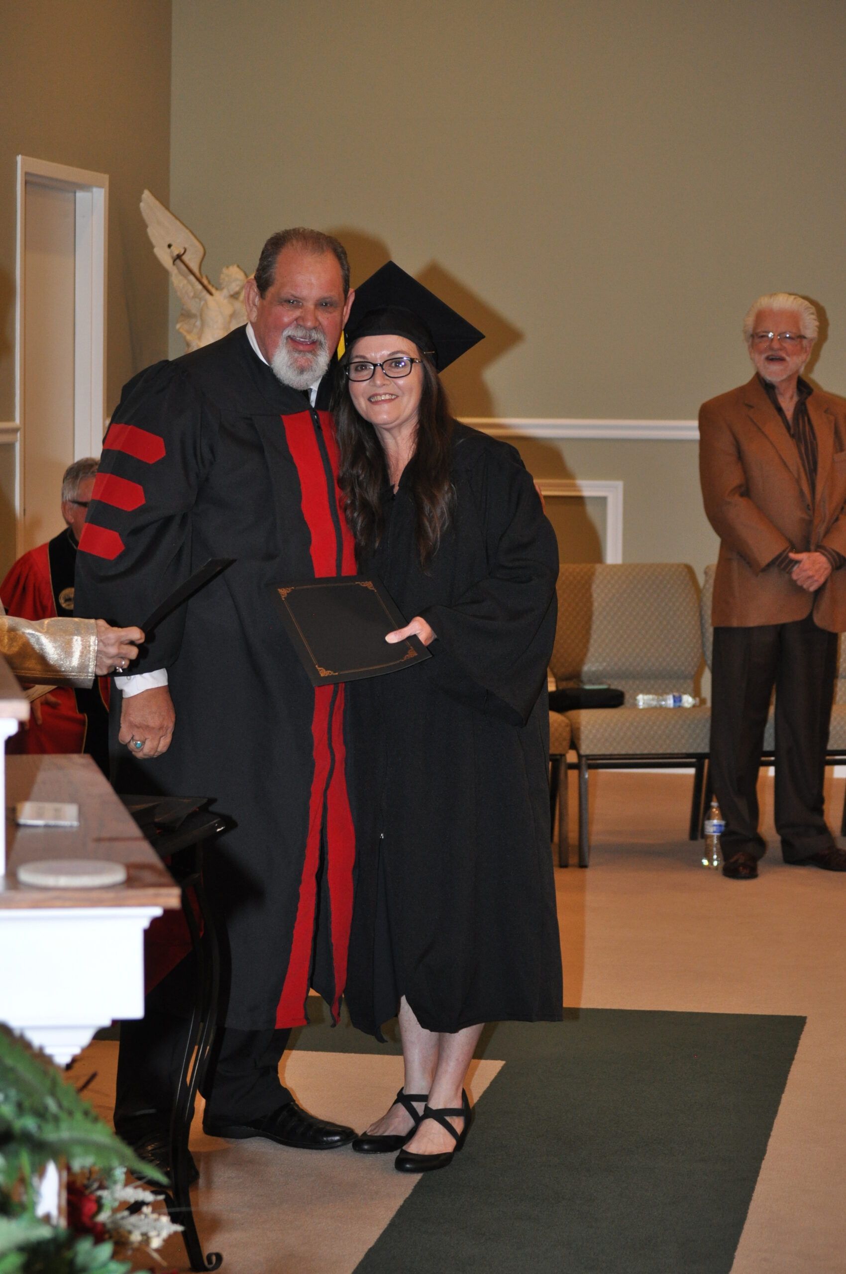 Person in graduation gown receives diploma from robed person, indoors.