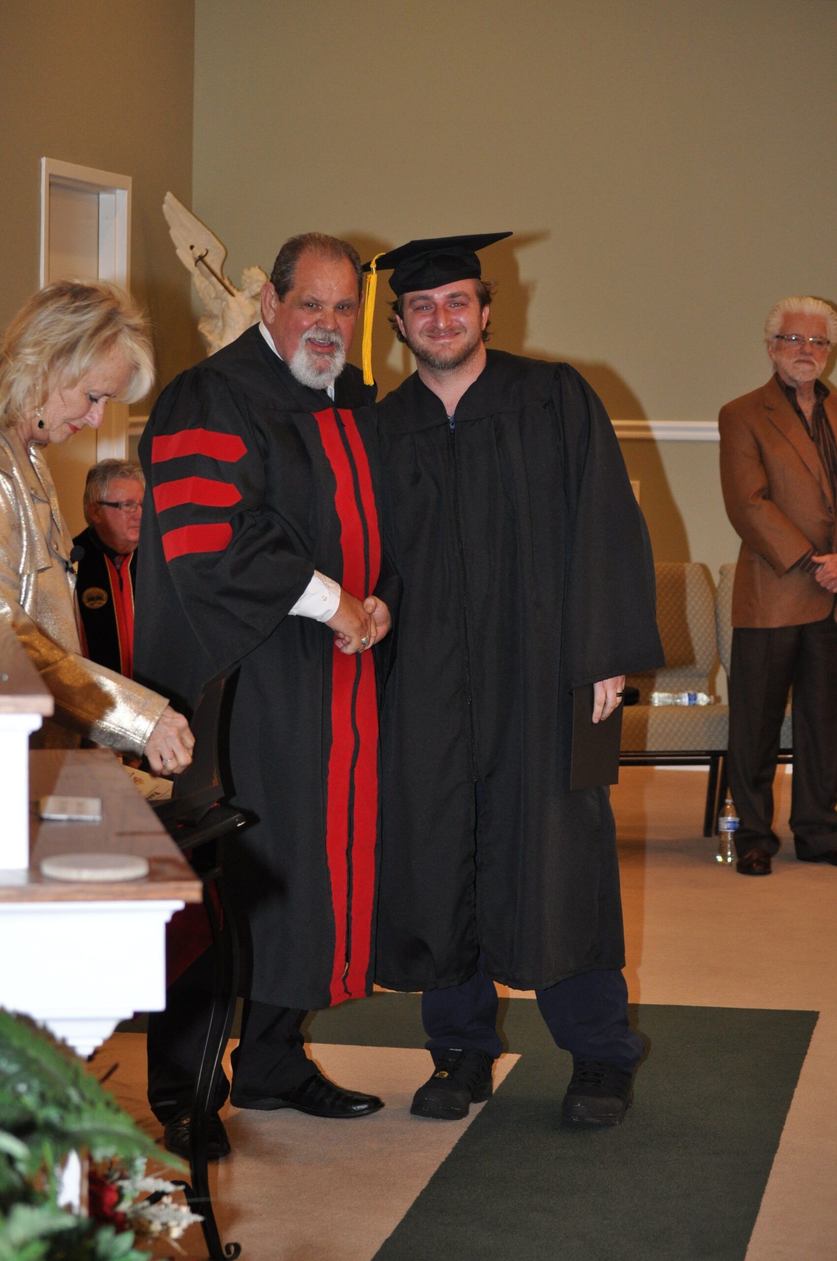 Man in graduation cap and gown poses with another man in academic robes at a ceremony.
