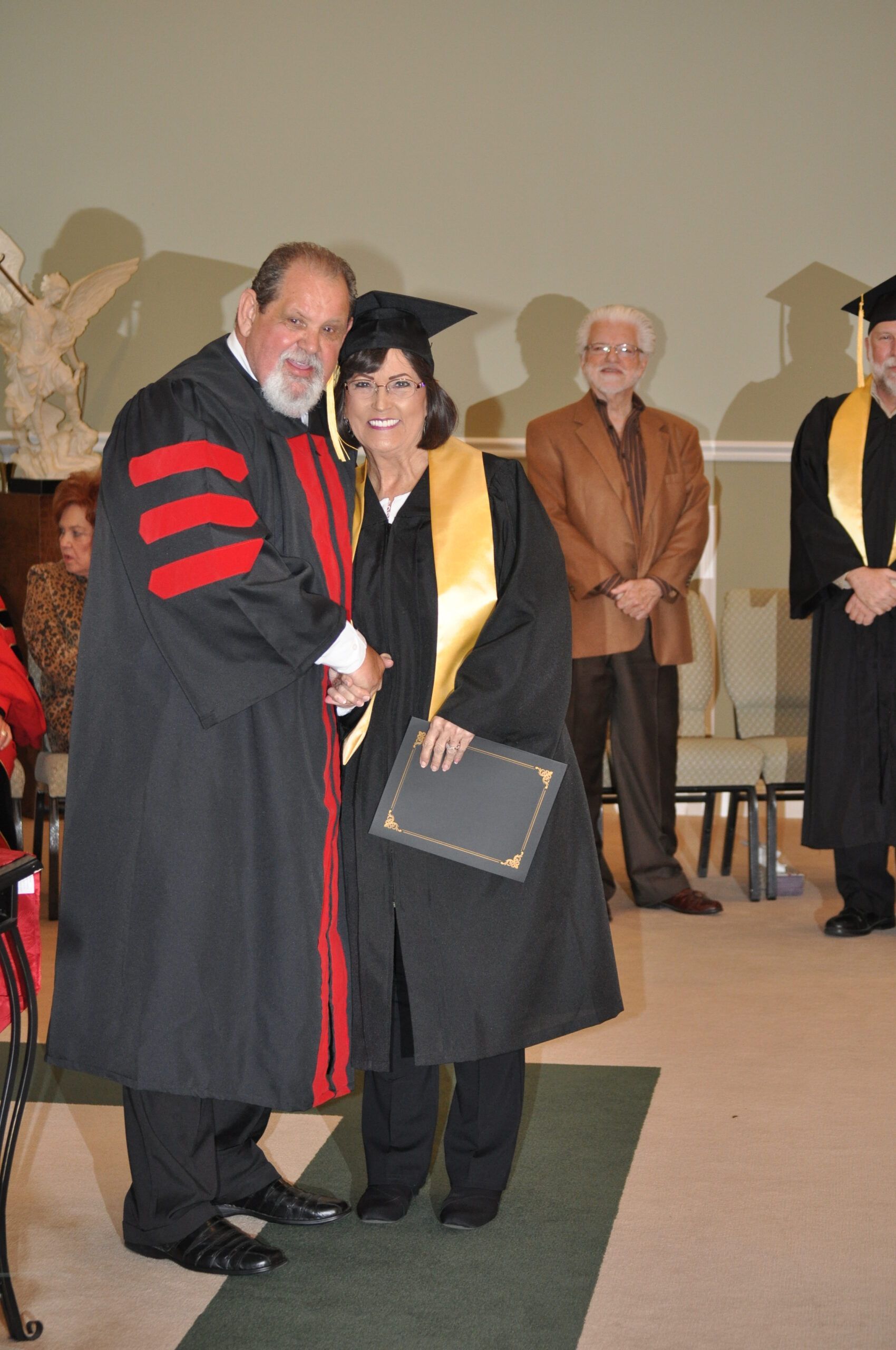 Person in graduation gown shaking hands with another person in a graduation gown.