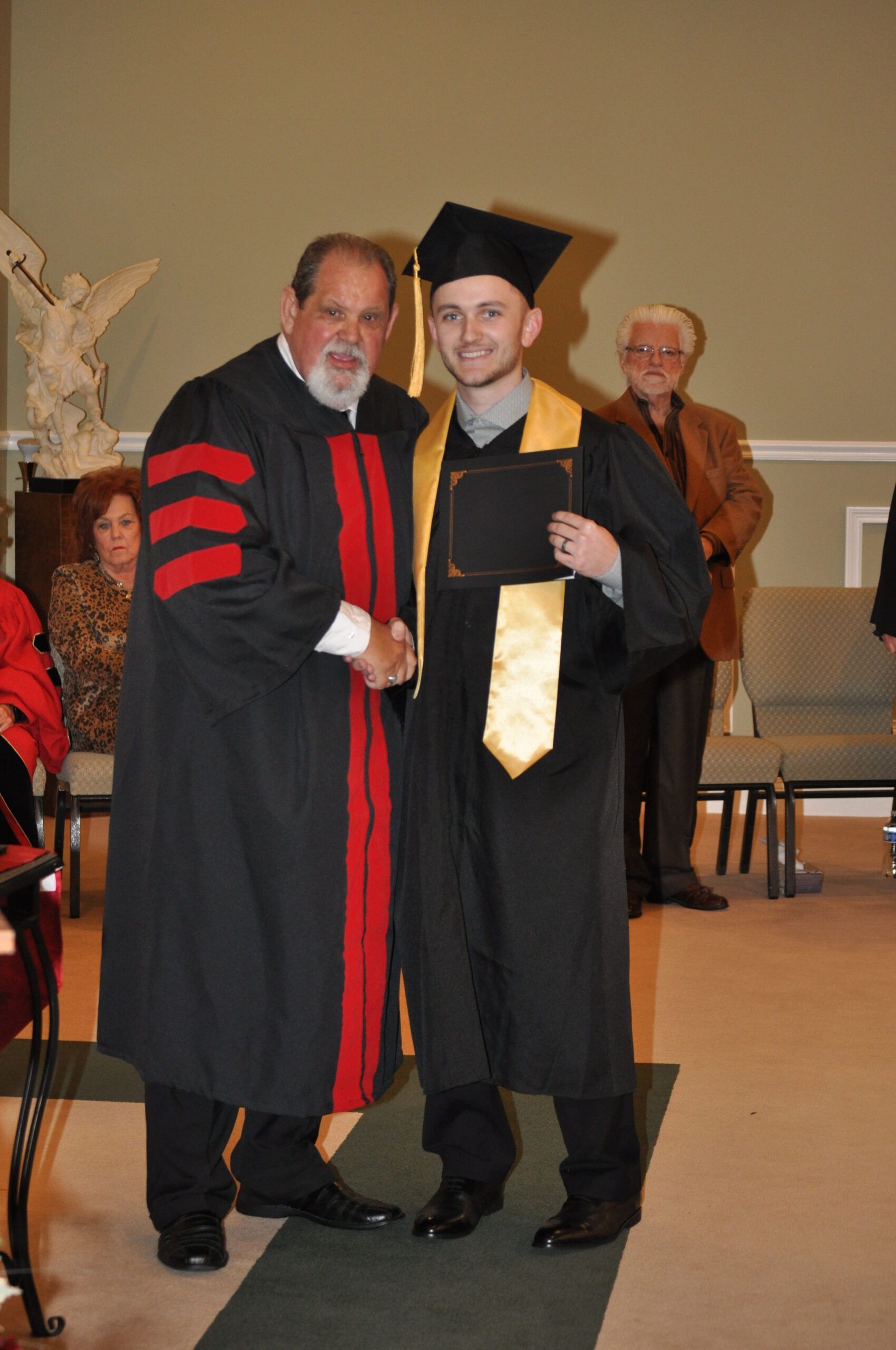 Man in cap and gown shakes hands with a man in academic regalia, graduation ceremony.