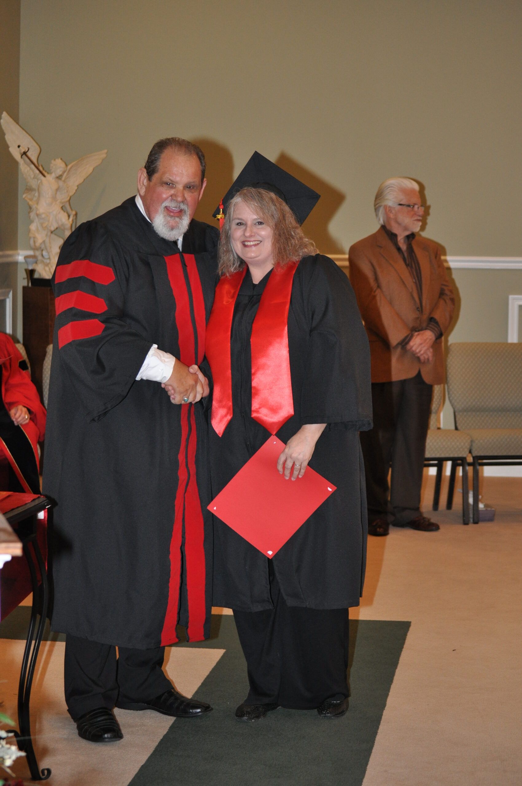 Man in academic robe shakes hands with graduate wearing cap and gown.