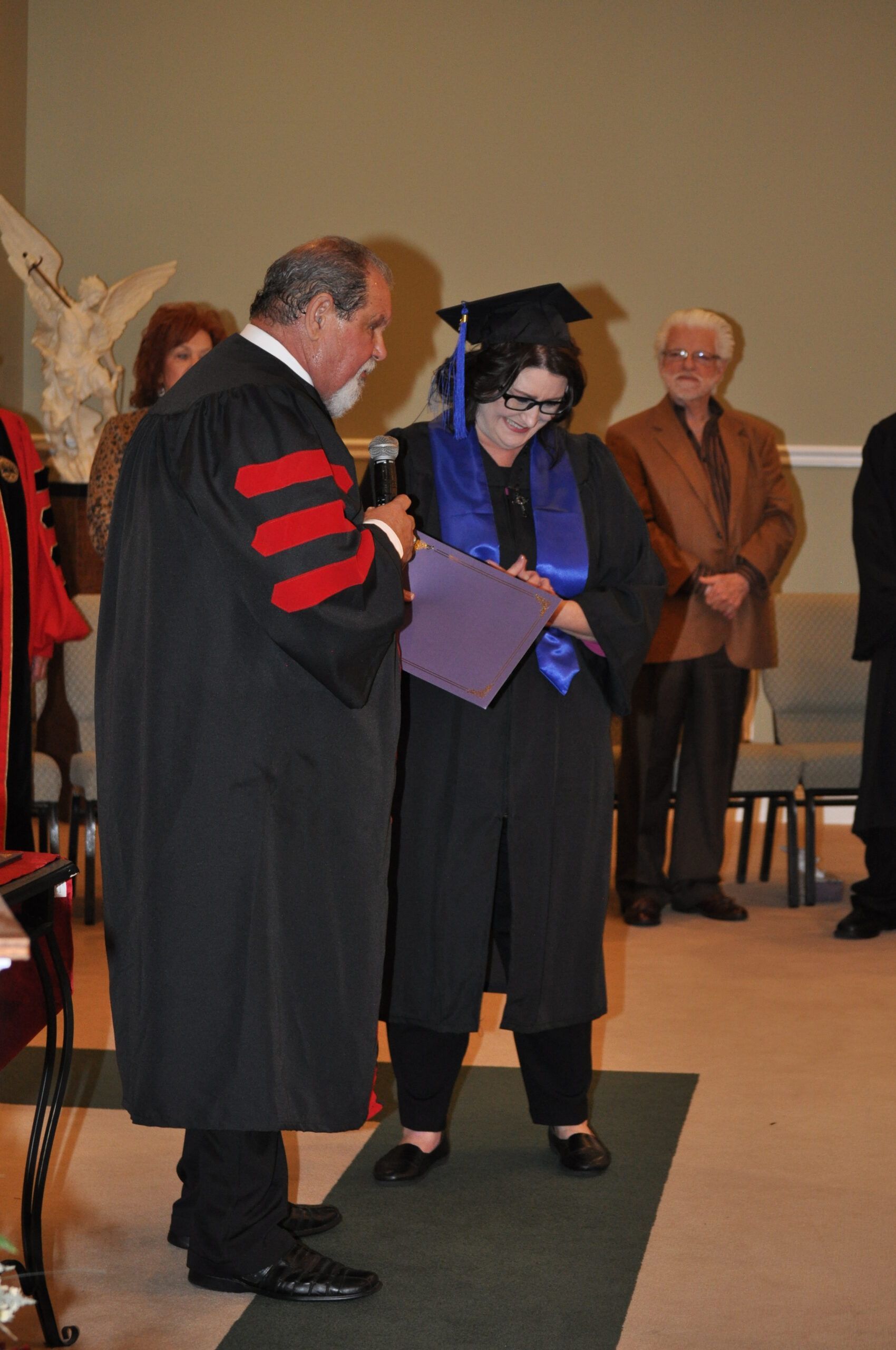 A graduate in cap and gown receives a diploma from a robed official at a ceremony.