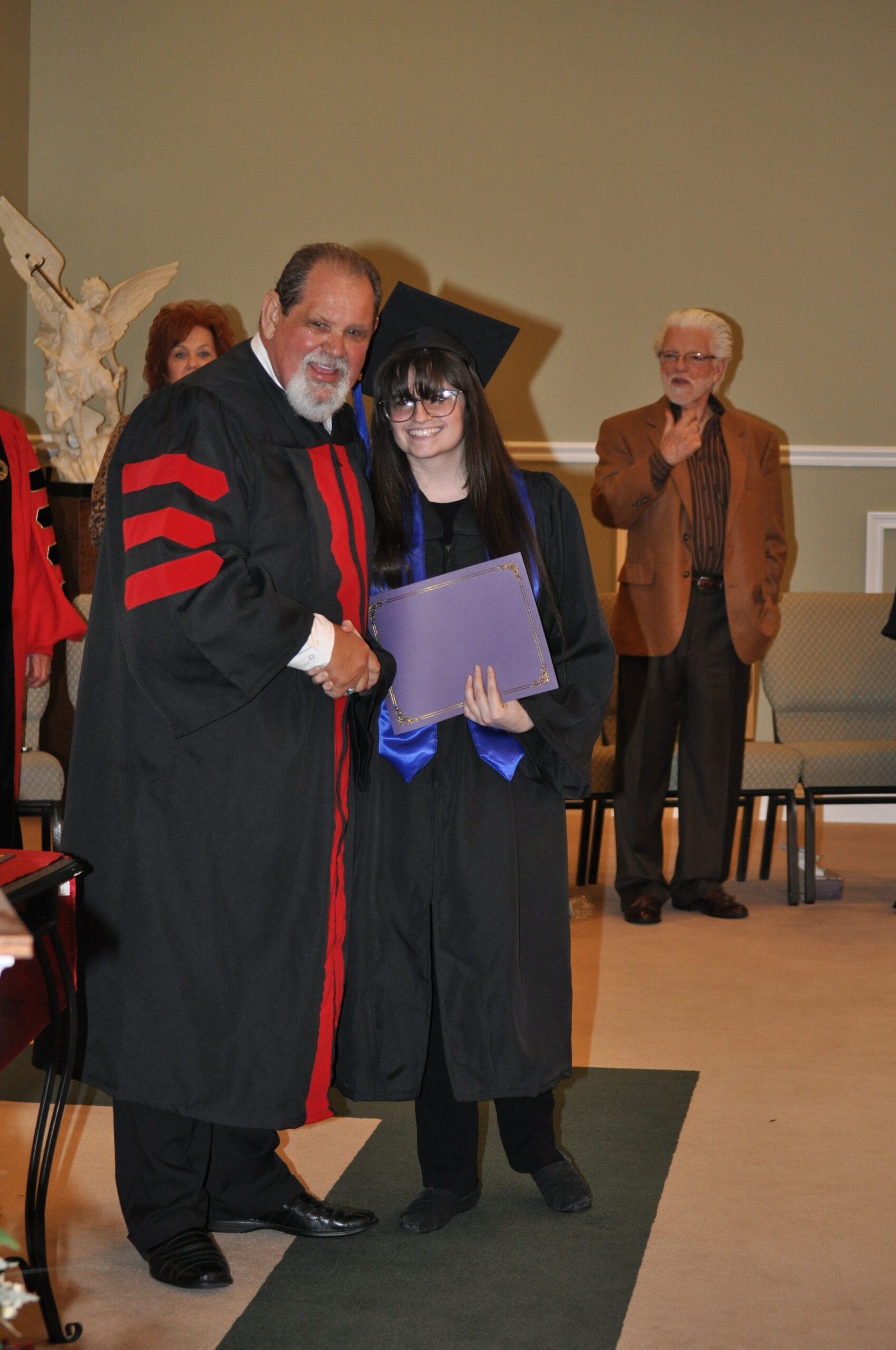 Person in graduation cap shaking hands with person in academic robe indoors.
