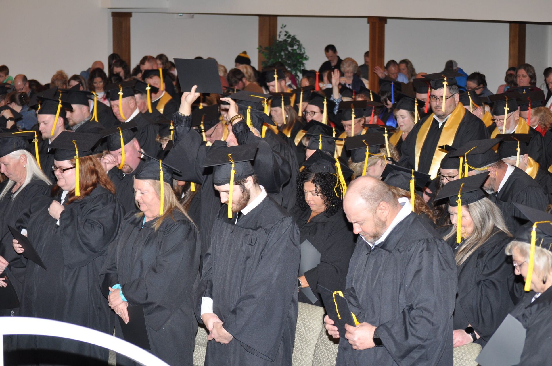 Graduates in black gowns and caps, some with yellow stoles, inside a building.