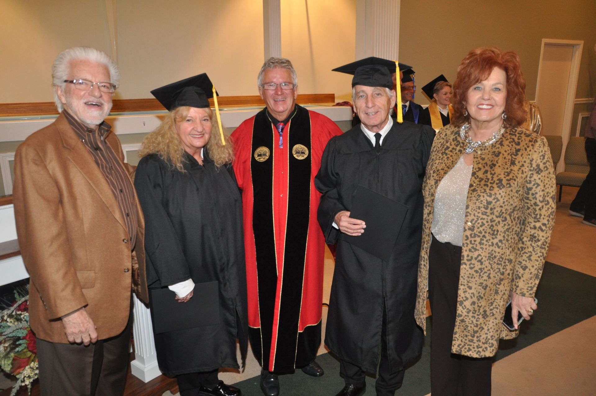 Group of people in graduation attire, smiling inside a building.