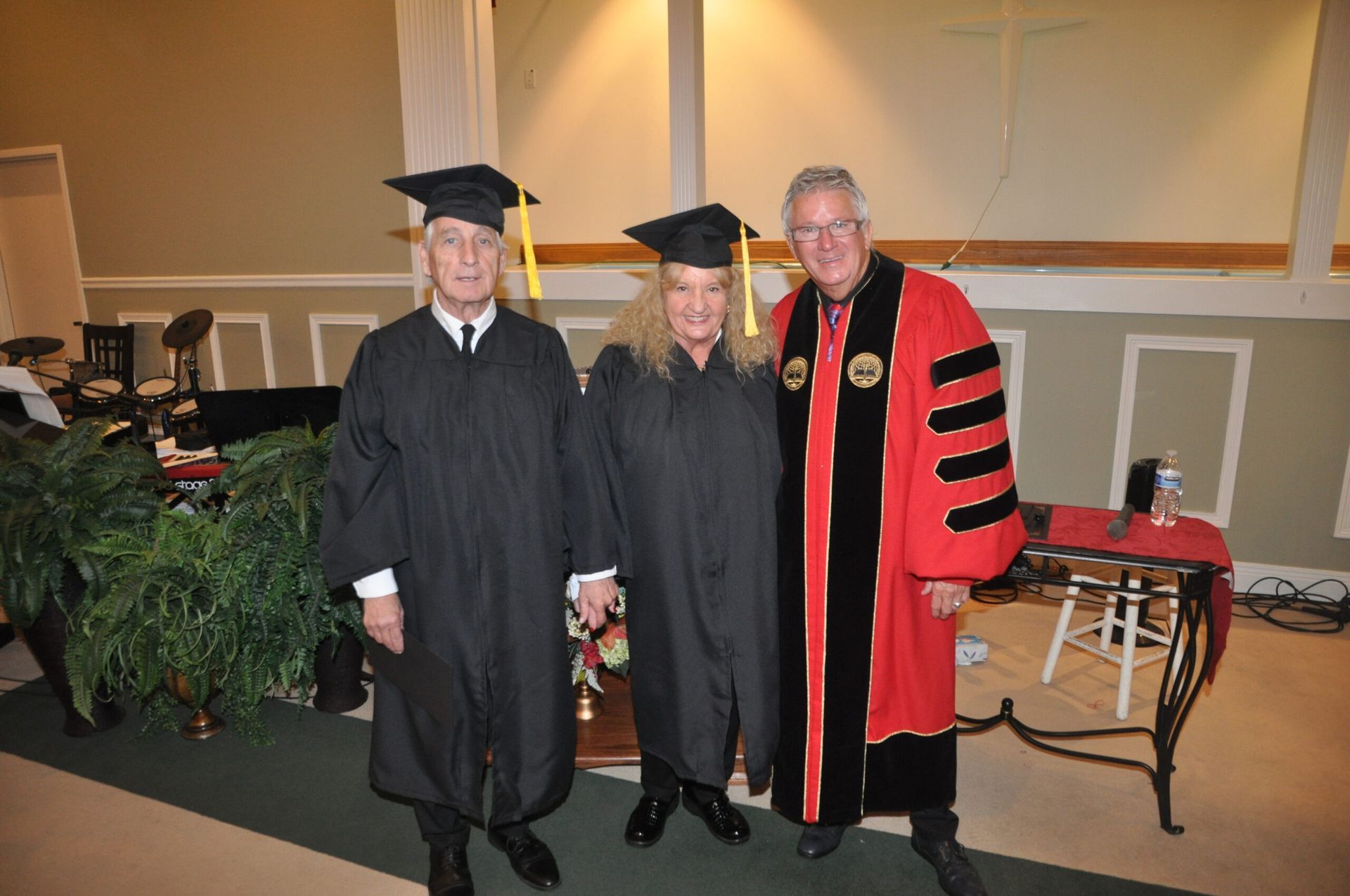 Three people in graduation attire pose in front of a church backdrop.