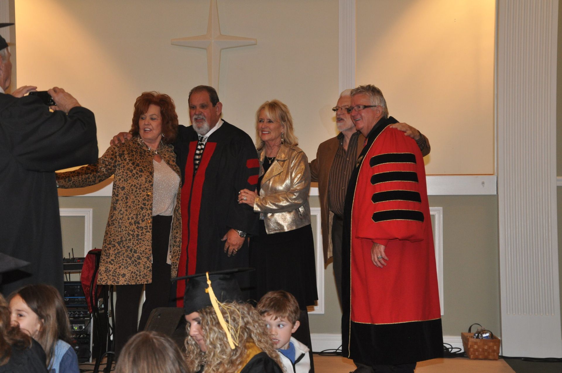 Group poses for photo during graduation. Red and black robes, formal attire, smiles.