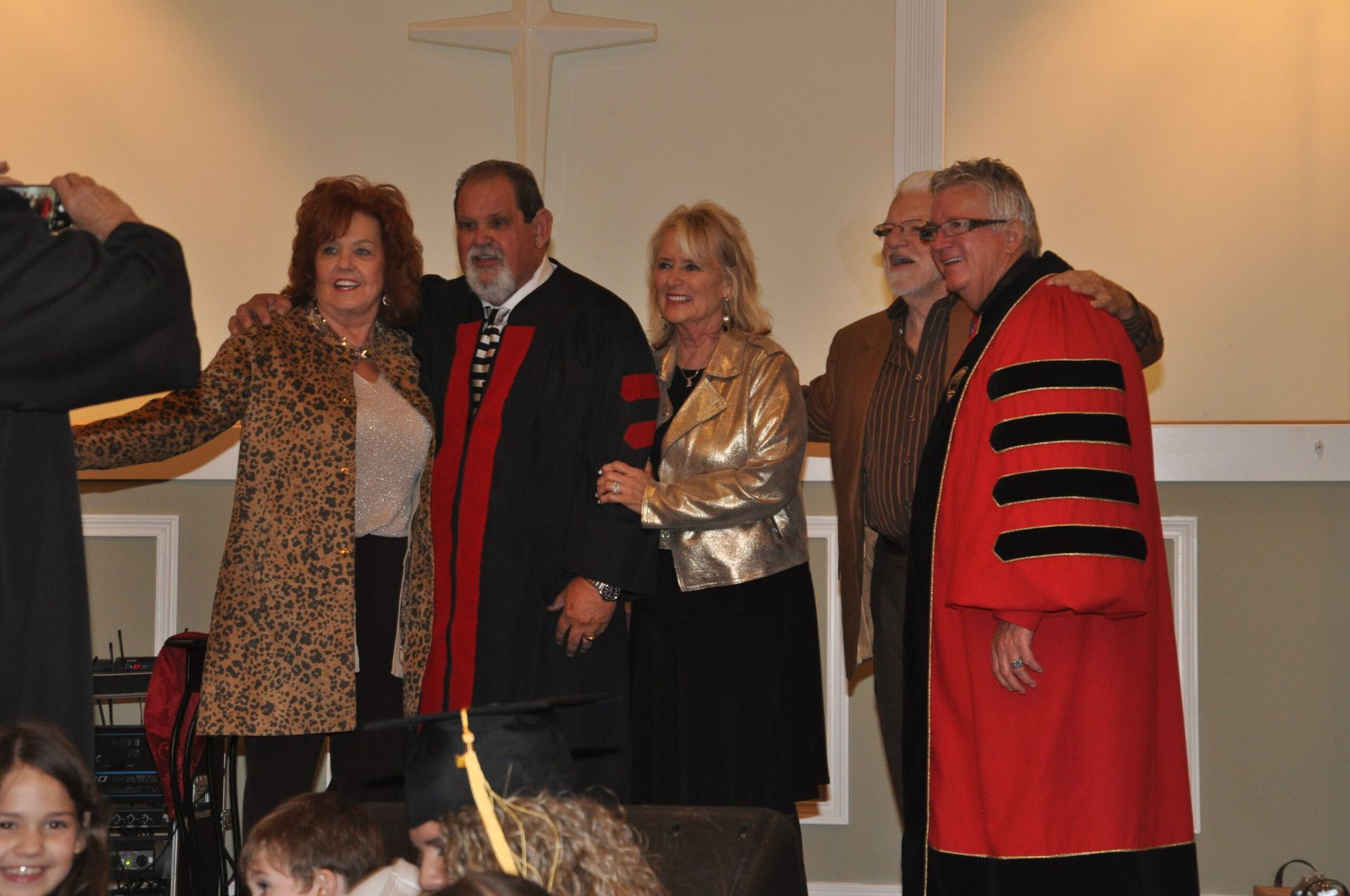 Group posing with robed individuals in a church with a cross on the wall.