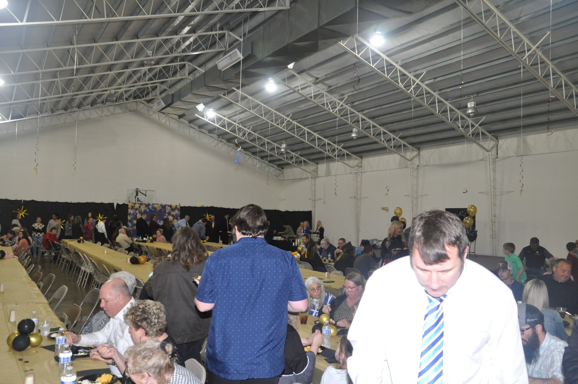 Large indoor event with tables, people seated, and a high ceiling.