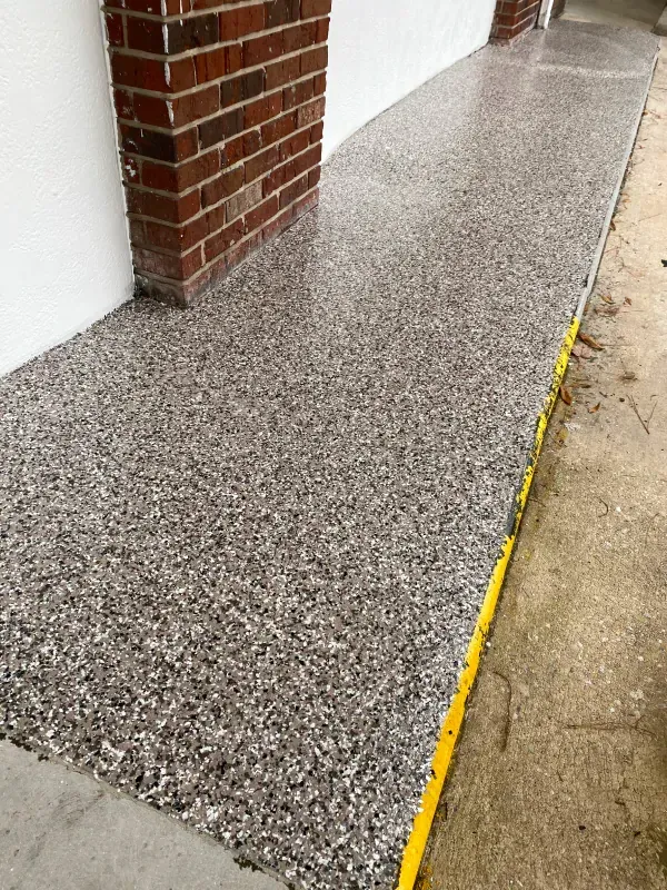 A long, textured concrete walkway with a brick pillar on the left and a yellow edge on the right.