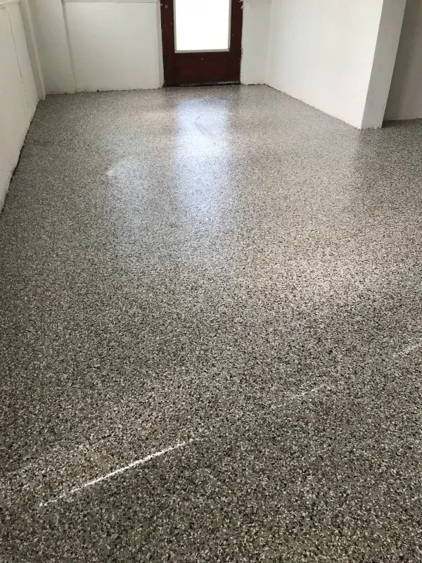 A room with a speckled, shiny gray and white floor, with a brown door at the back.