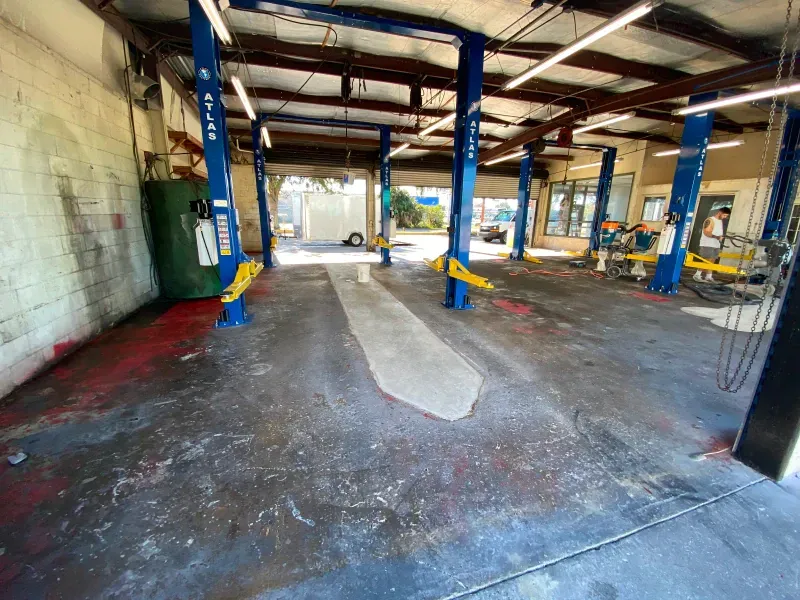 Empty auto repair shop interior with blue car lifts, concrete floor, and open doors to the exterior.