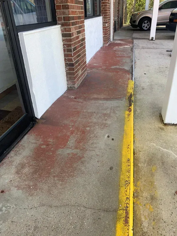 A concrete sidewalk with faded red paint, a yellow curb, and a brick wall.