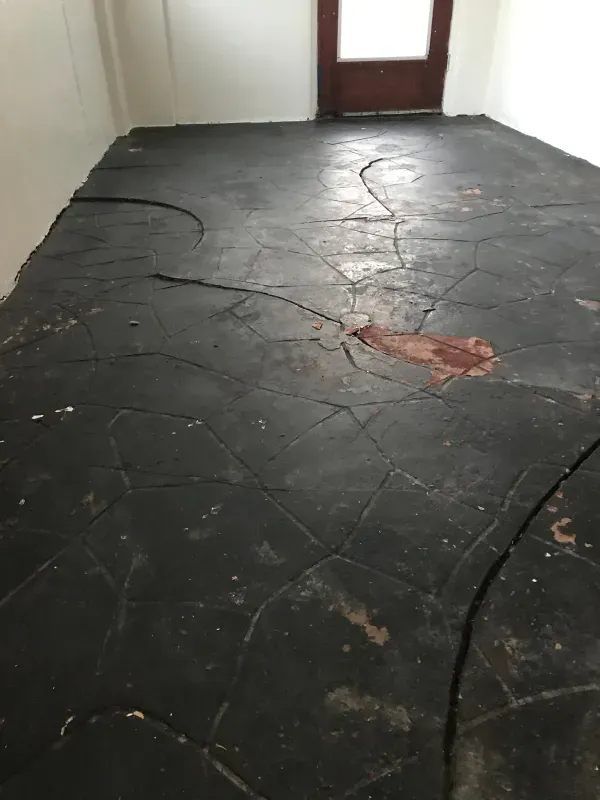 Black textured floor with cracks and a reddish-brown stain in a room.