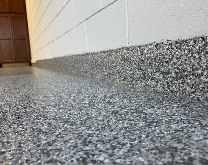 Close-up of a speckled gray flooring and baseboard against a white cinder block wall in a hallway. Close-up of a speckled gray flooring and baseboard against a white cinder block wall in a hallway.