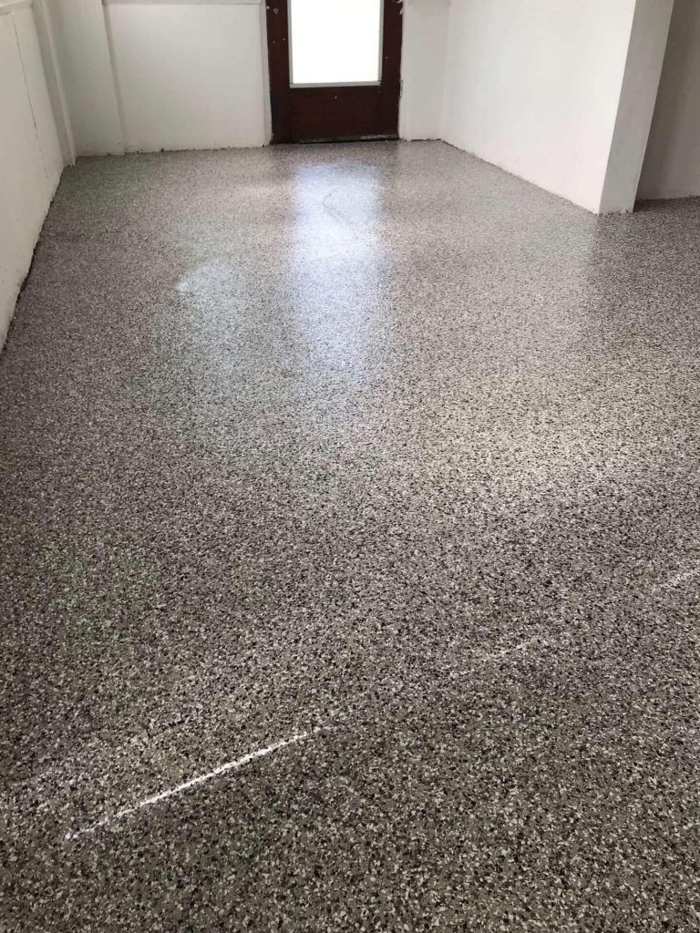 A newly finished epoxy-flake floor in a room with white walls and a dark wooden door.