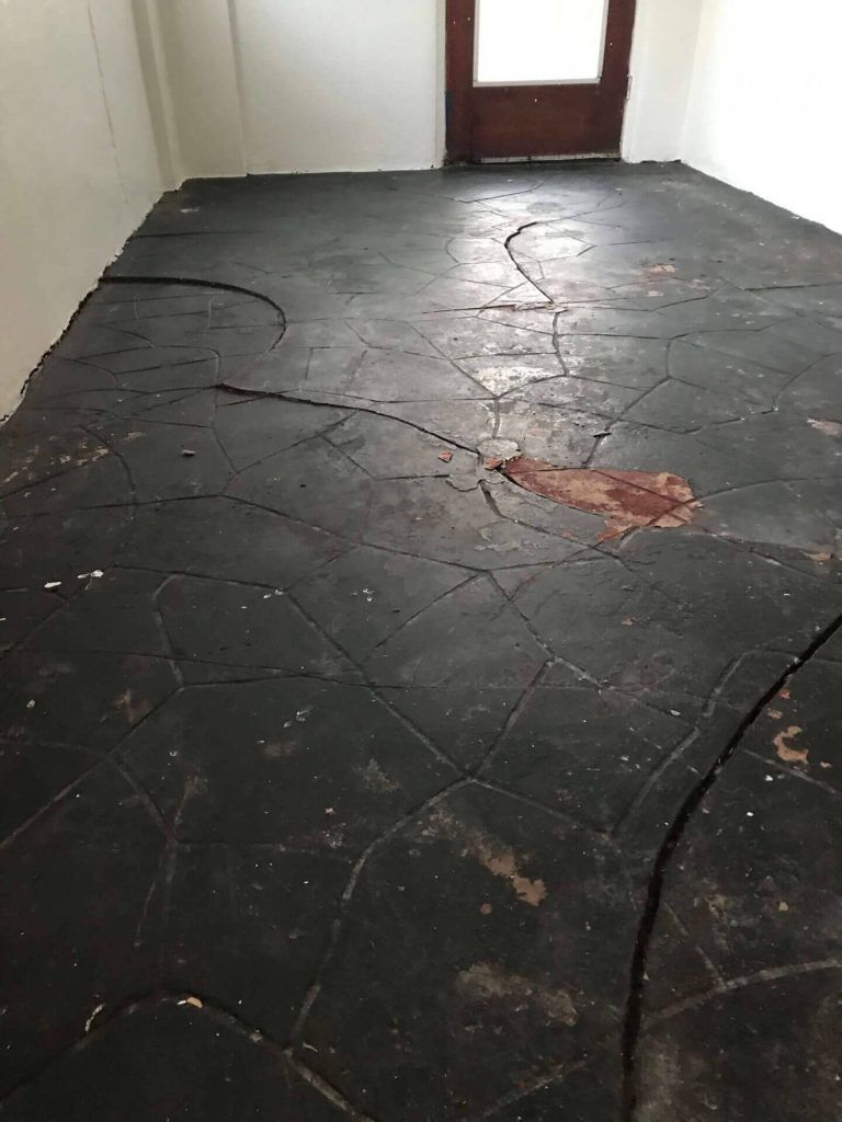Dark, cracked floor in a room with white walls and a wooden door.