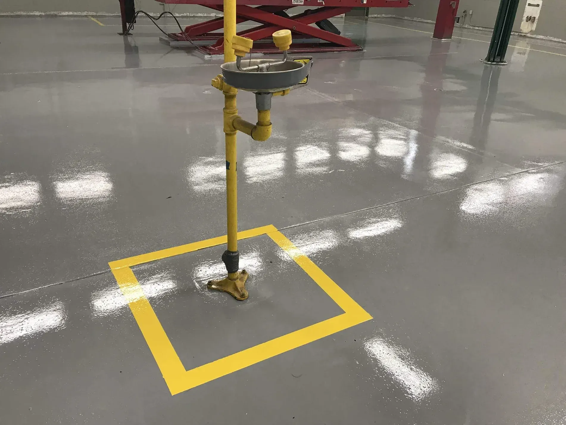 Yellow emergency shower station on a gray floor, outlined with a yellow square. Yellow emergency shower station on a gray floor, outlined with a yellow square.