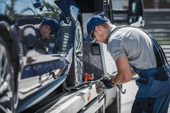 man tightening chain to ensure car is strapped onto flatbed tow truck