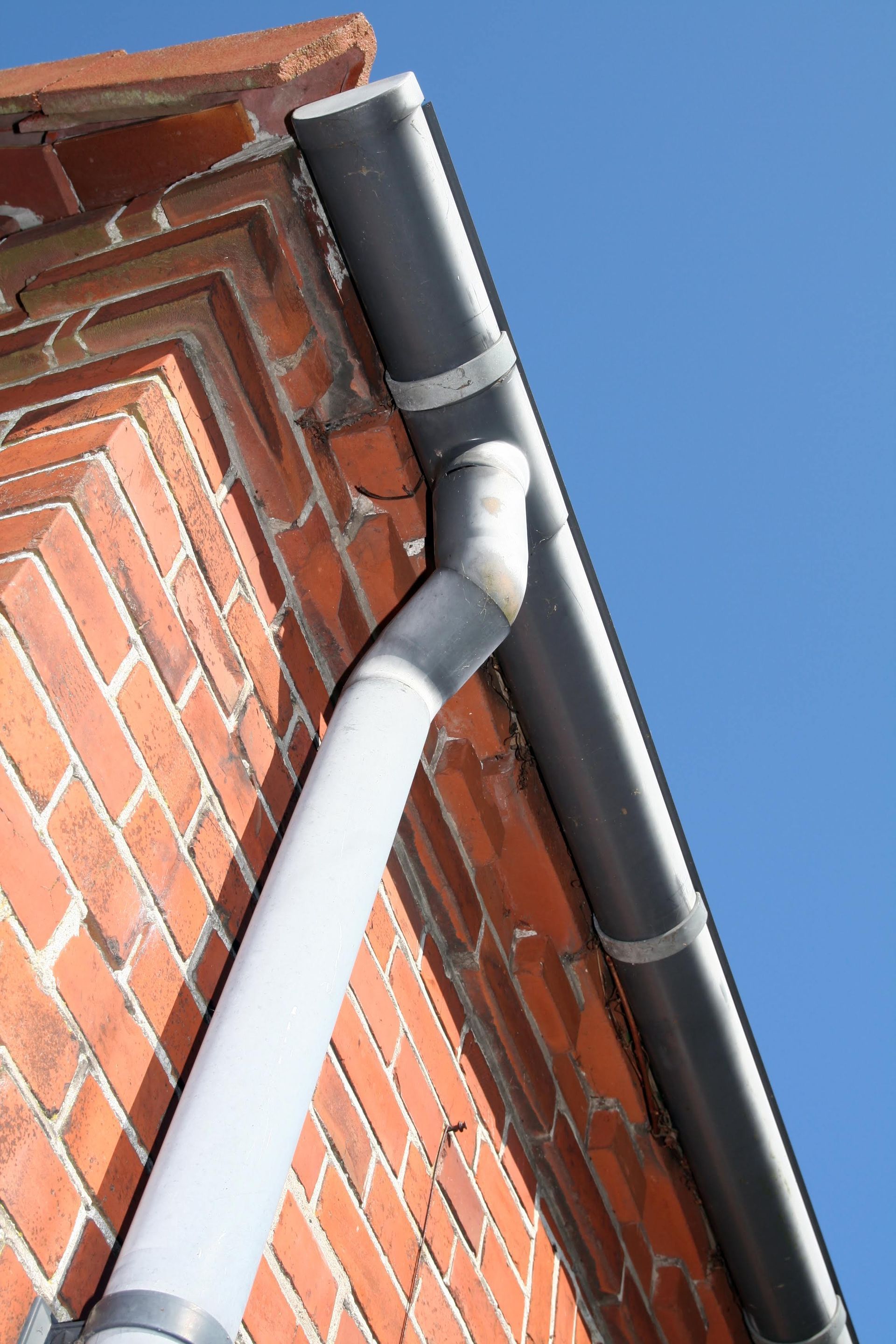 A gutter on the side of a brick building with a blue sky in the background.