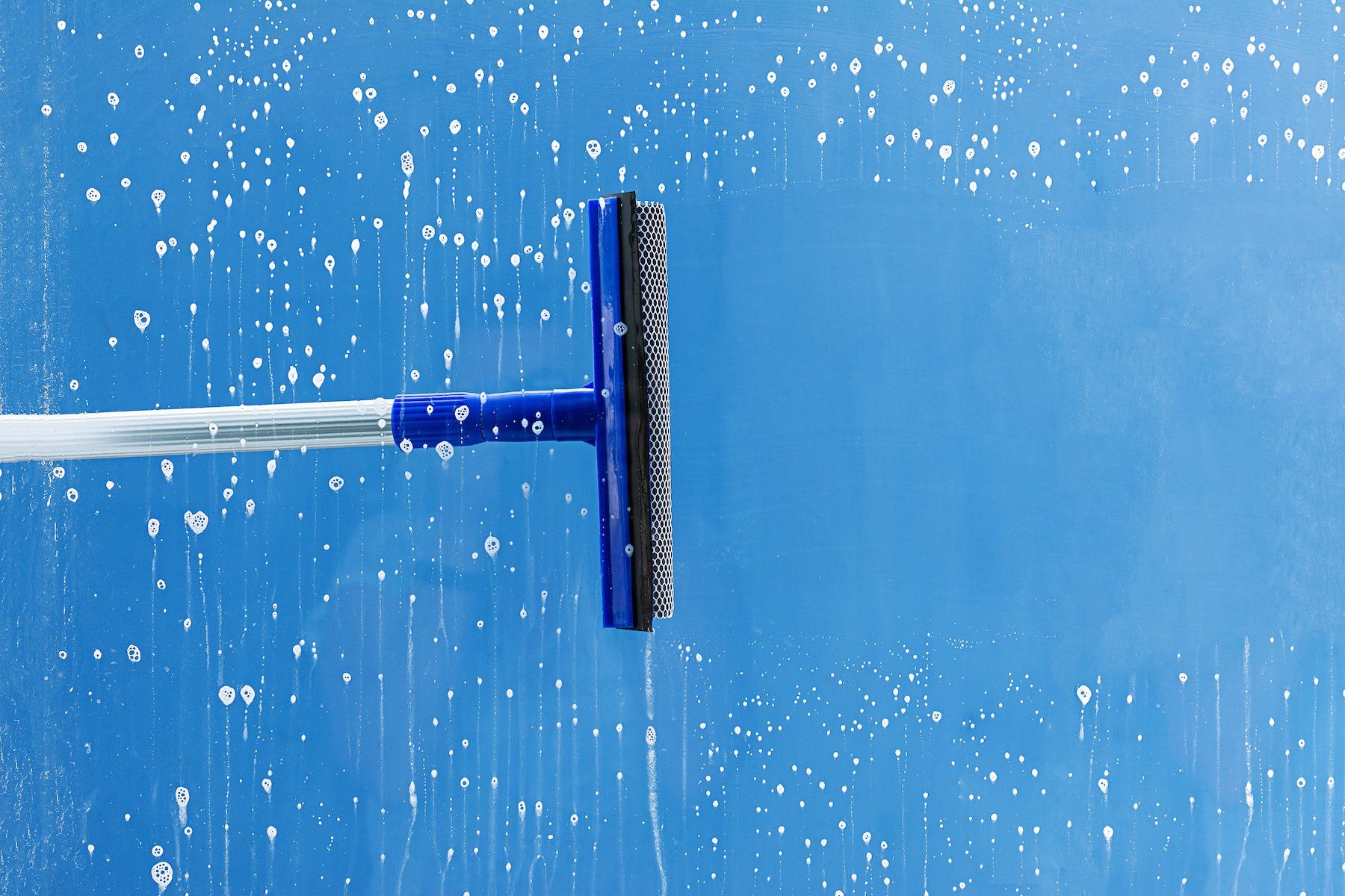 A blue squeegee is being used to clean a window.