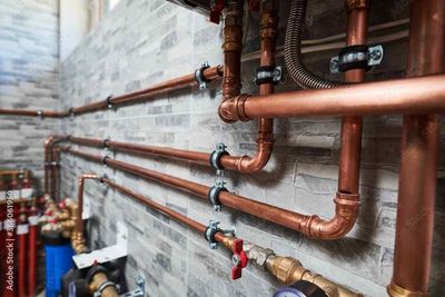 A bunch of copper pipes are hanging on a brick wall.