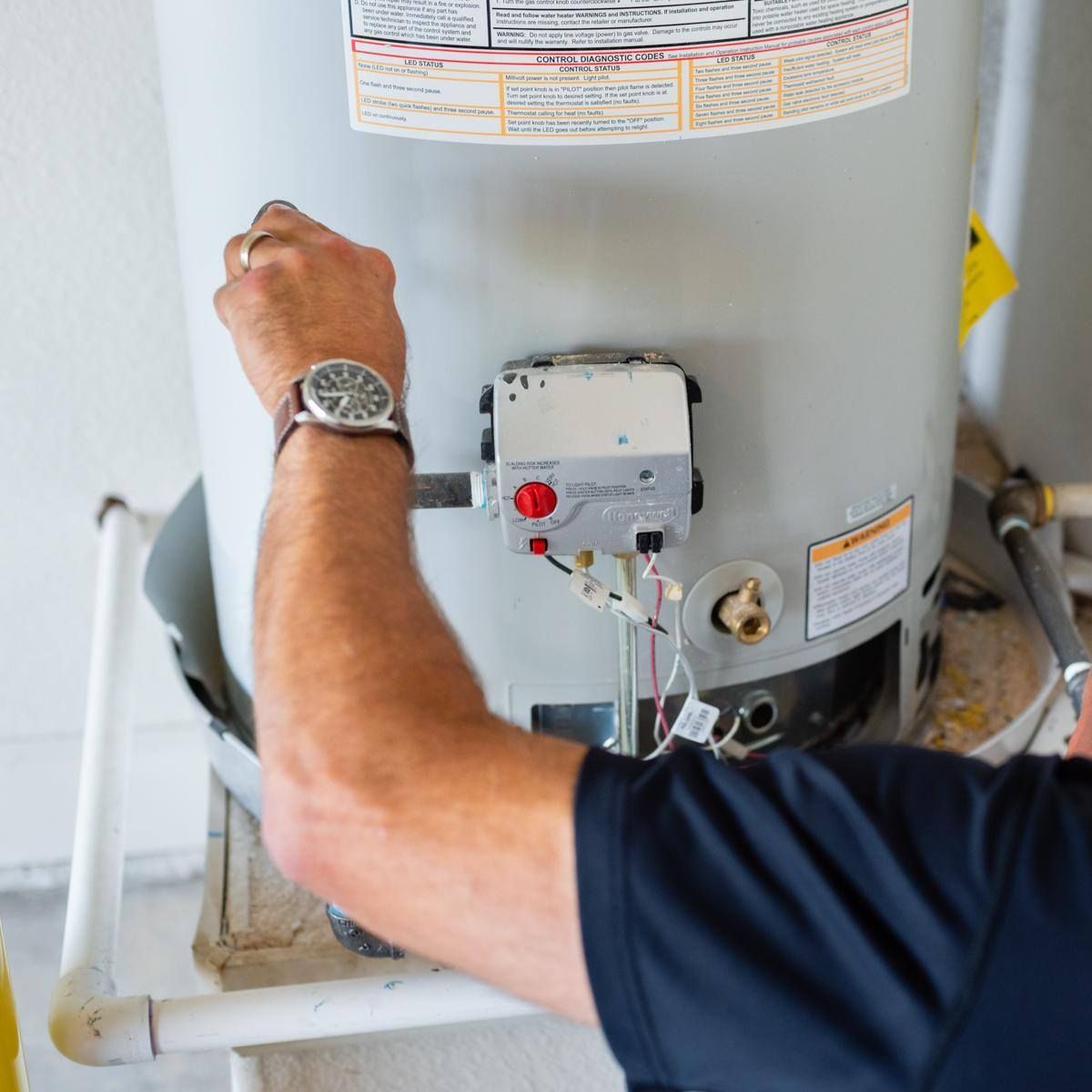 A man wearing a watch is working on a water heater.