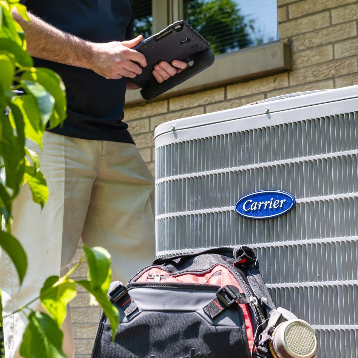A man holding a tablet next to a carrier air conditioner