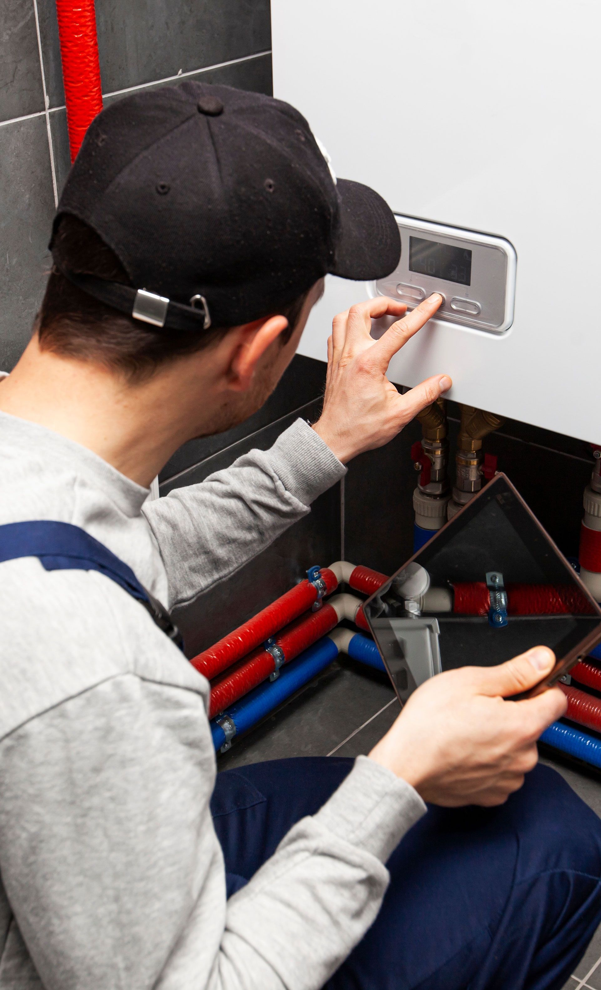 A man is working on a boiler in a bathroom while using a tablet.