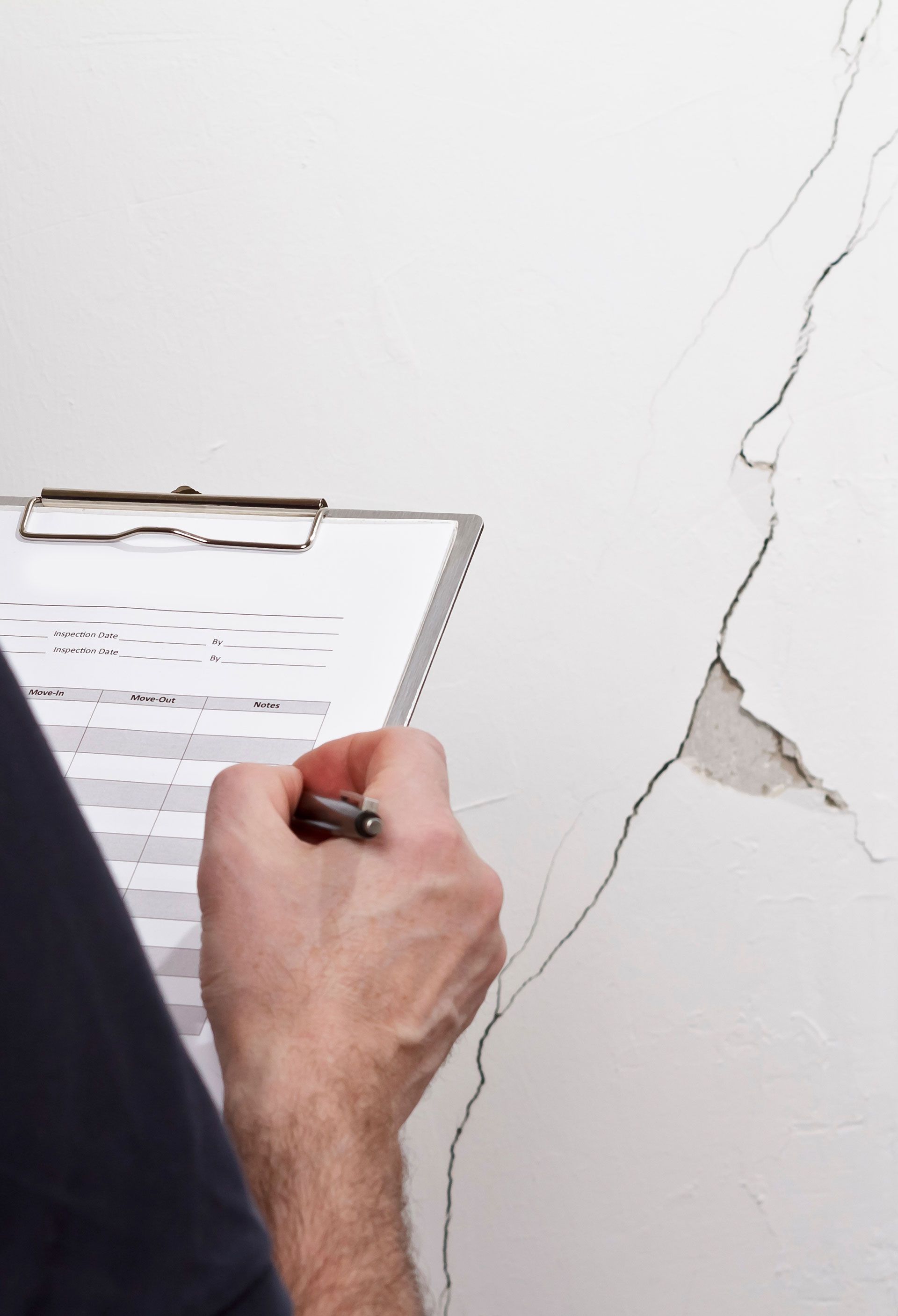 A person is writing on a clipboard in front of a cracked wall.