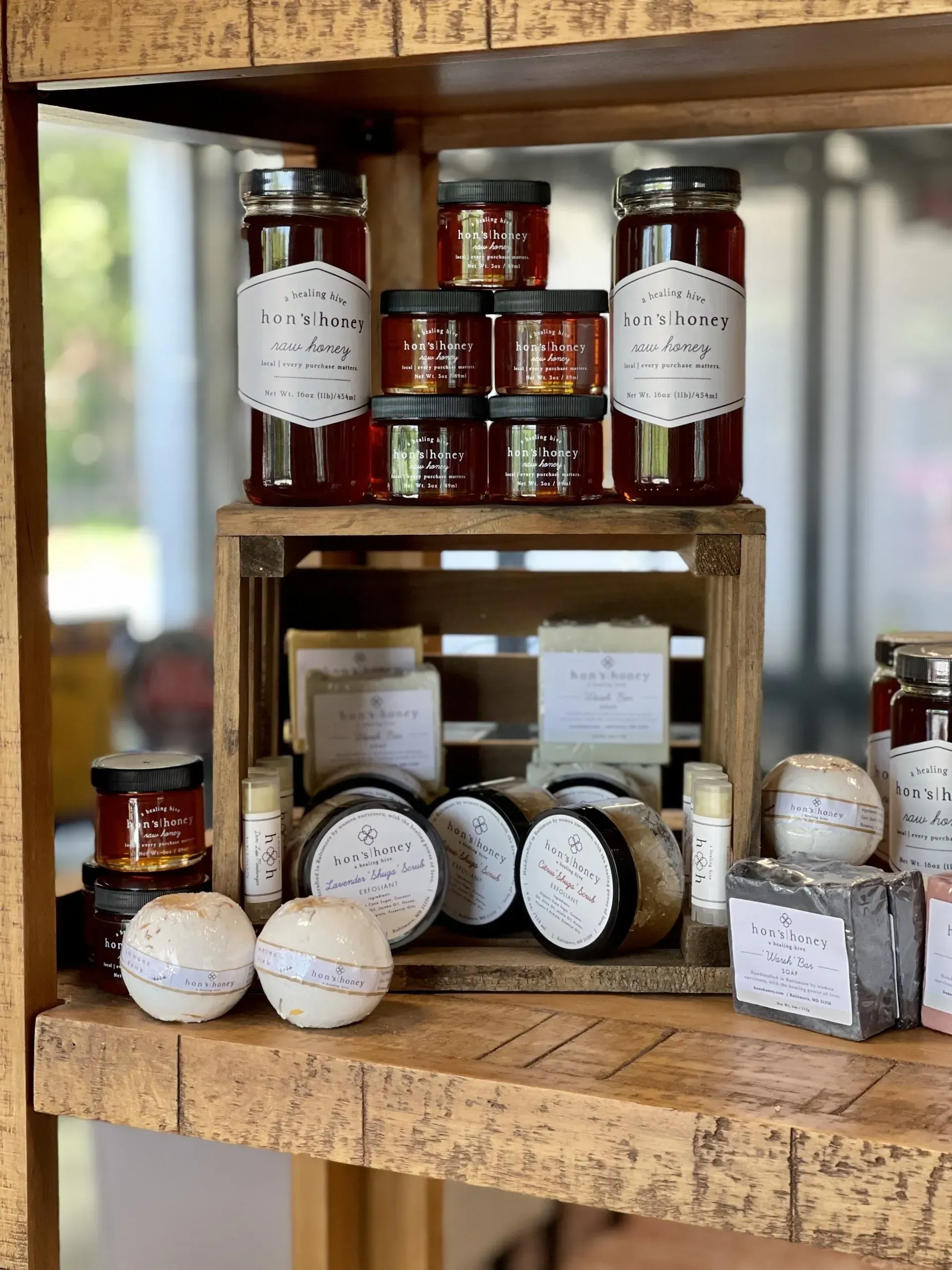 Shelves displaying jars of honey, soaps, and bath bombs. Wooden crate and shelving.