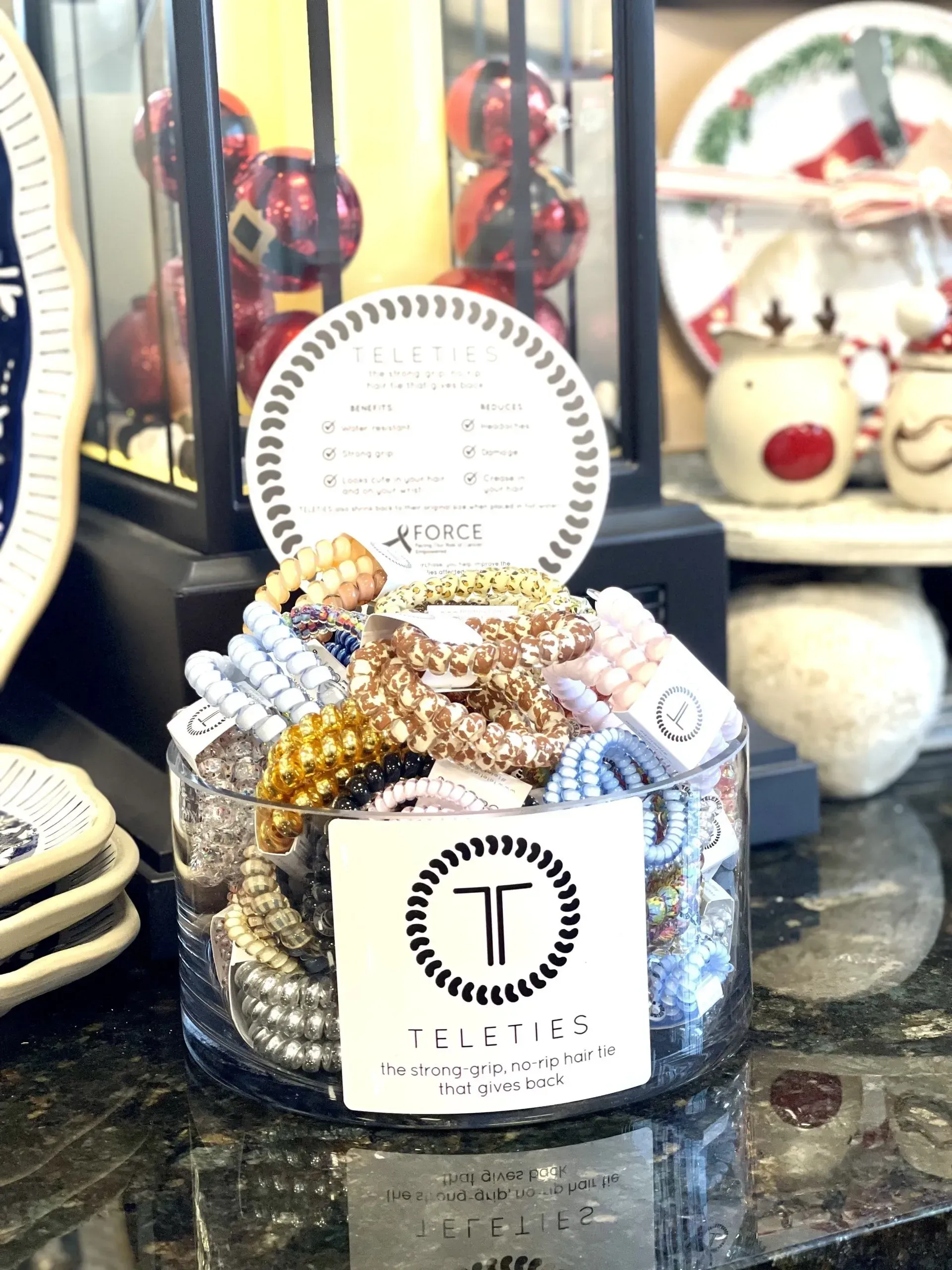 A clear jar filled with beaded bracelets on a counter, with a decorative sign and lantern in the background.