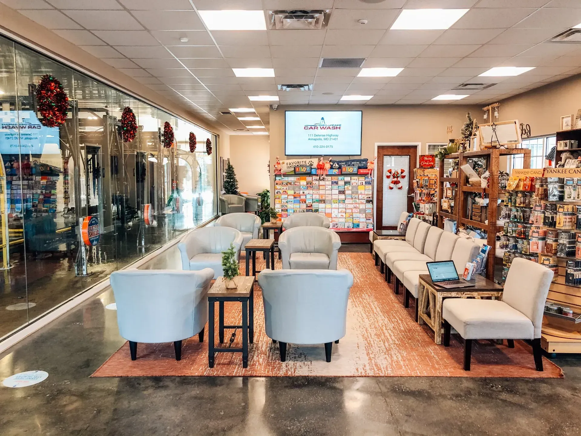 An indoor waiting area with seating, small tables, and a digital display. Storefront windows in the background.