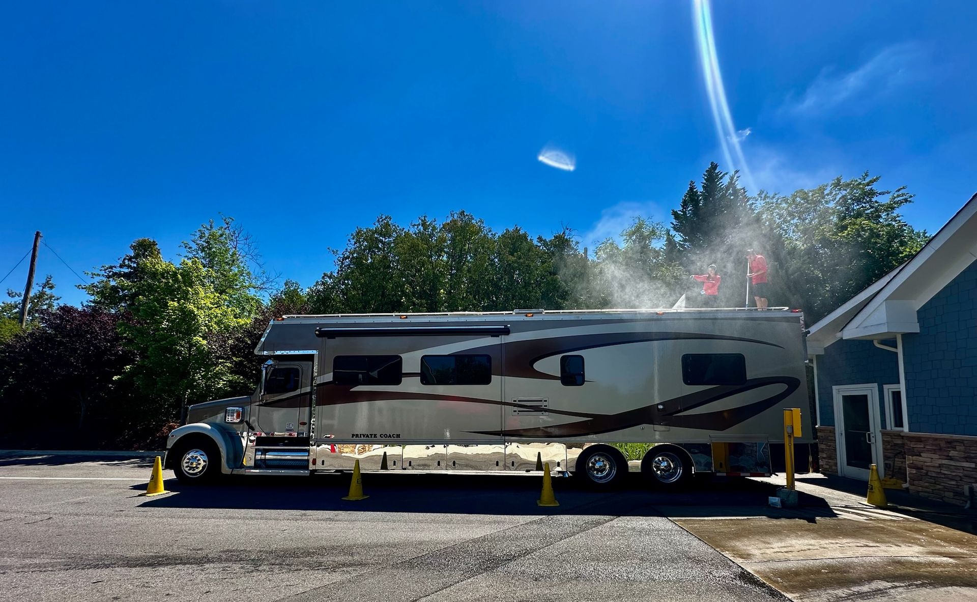 Large white-and-black RV parked beside a house under a bright blue sky