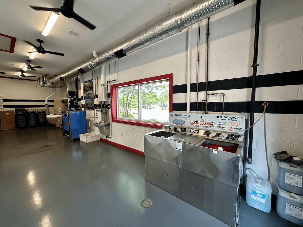 Spacious auto shop with tools, blue bins, black-striped walls, large red-framed window, and gray concrete floor