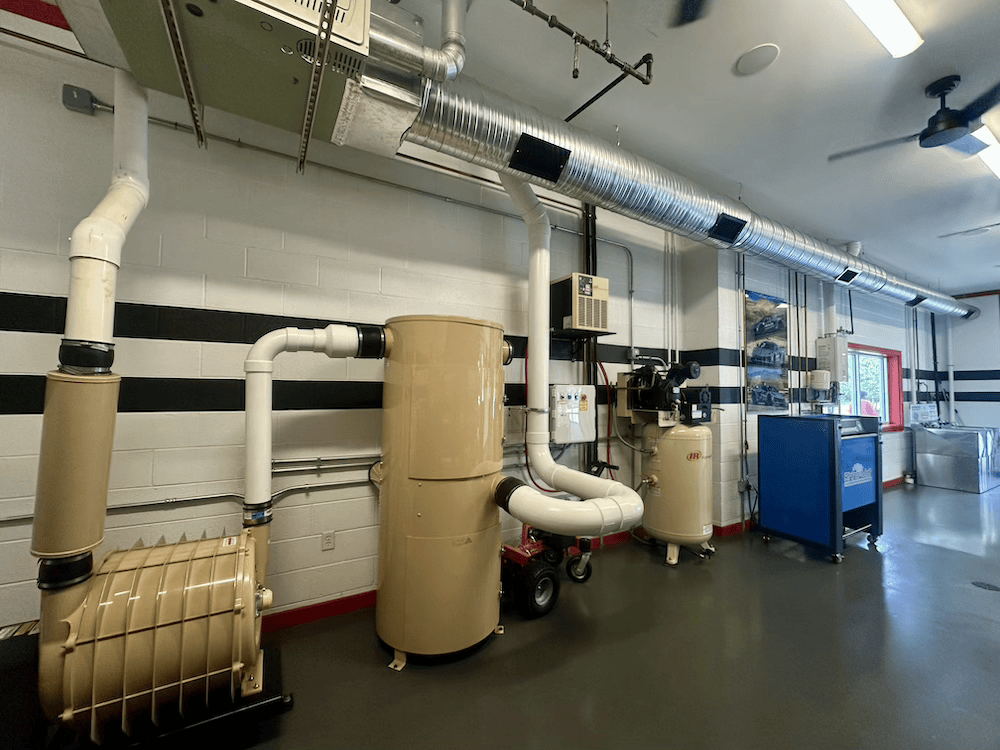 Industrial room with beige ductwork, pipes, and a blue equipment cabinet along a white wall.