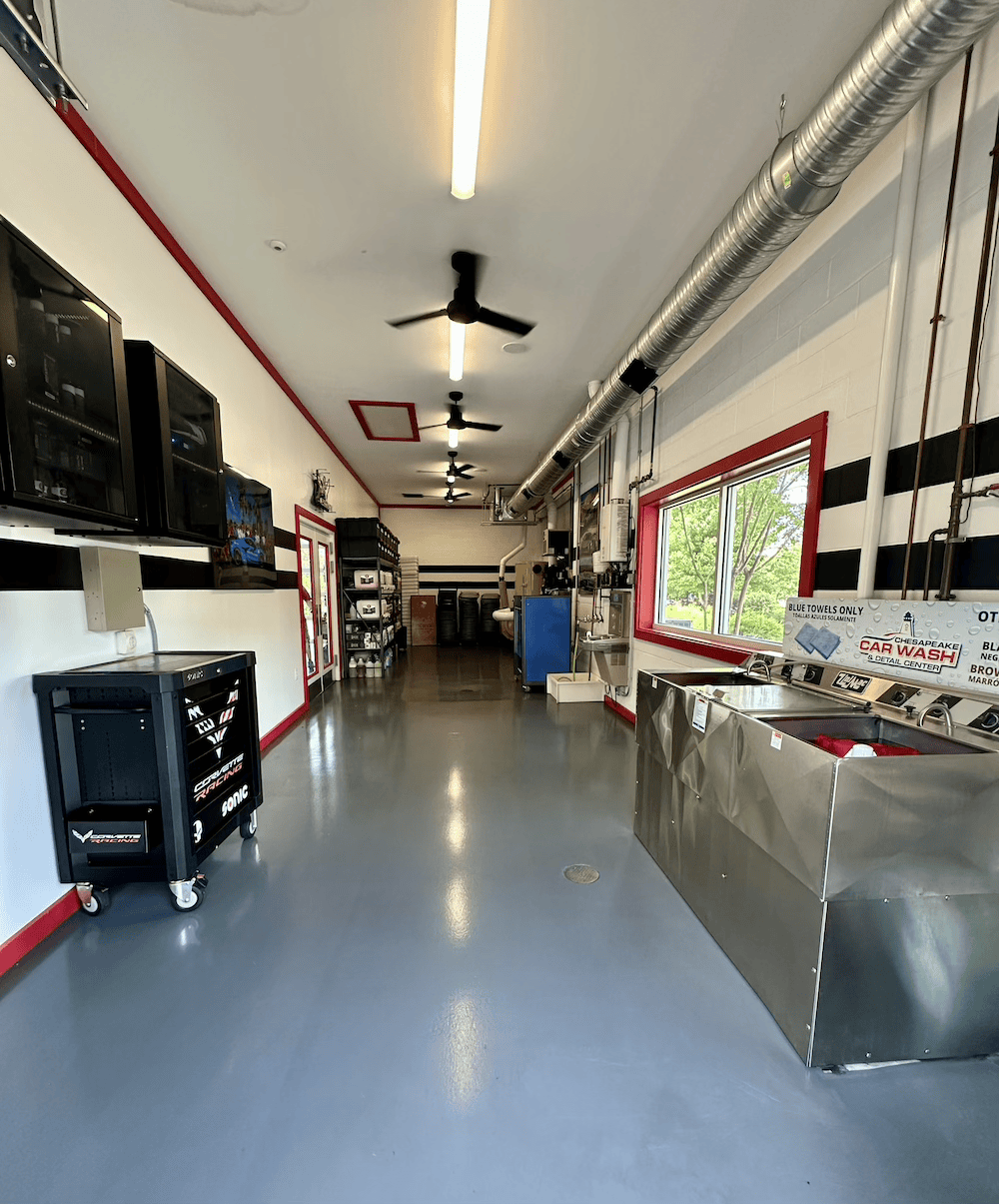Indoor workshop with metal counters, shelves, and ceiling fans, lit by bright overhead lights