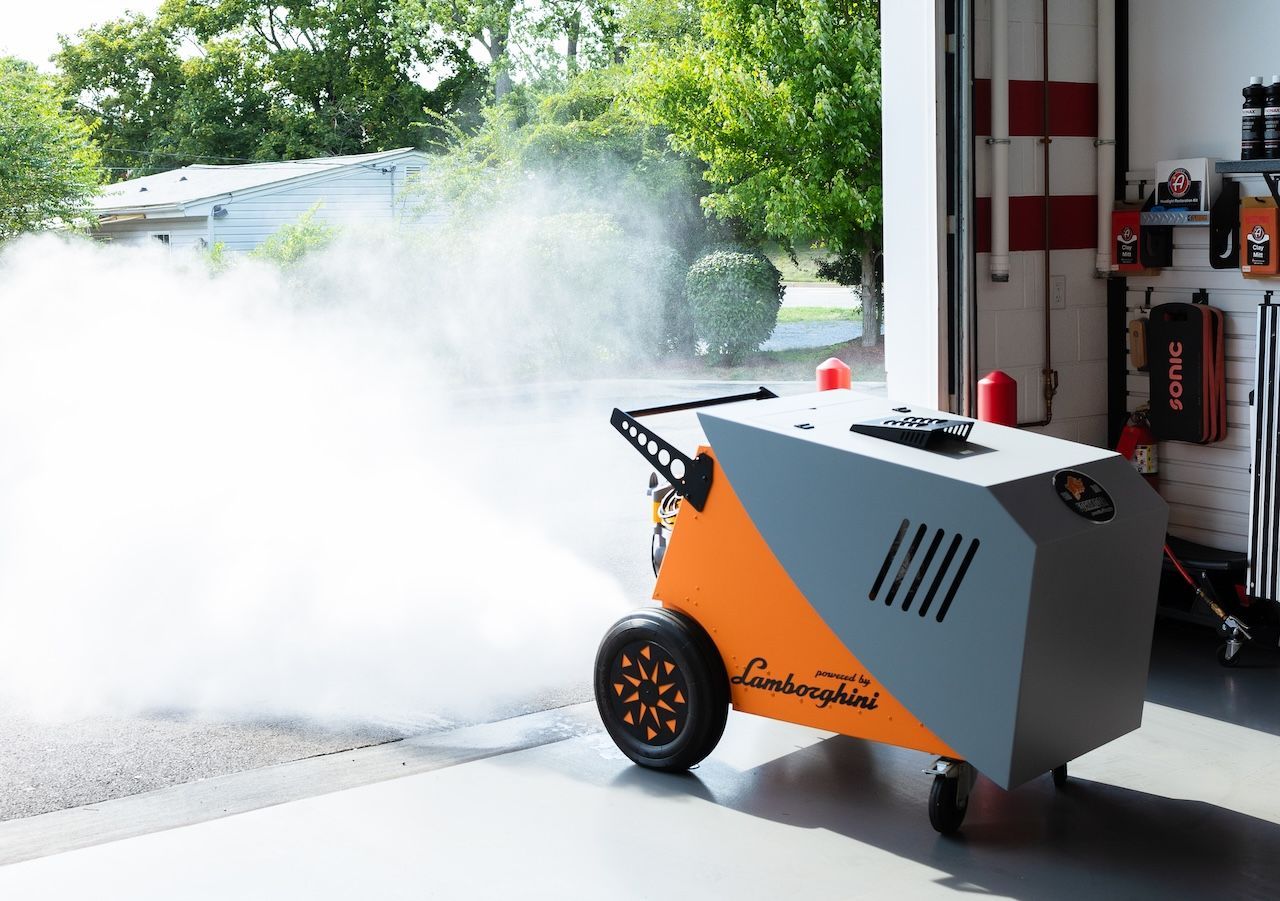 Orange fire-suppression machine spraying a dense white foam cloud in a garage bay