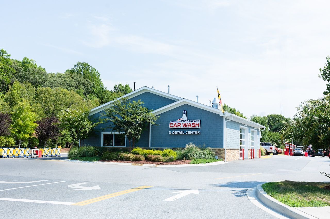 Blue building at a road intersection, surrounded by trees and landscaping under a bright sky.