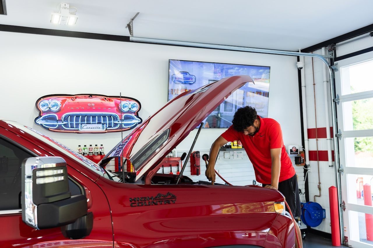 Person working under the hood of a red car in a garage