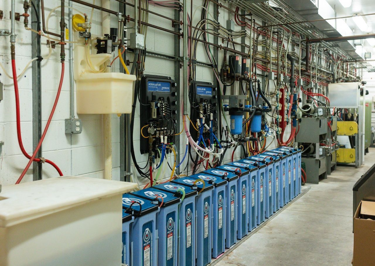 Industrial equipment room with rows of blue battery units, cables, and wall-mounted control panels