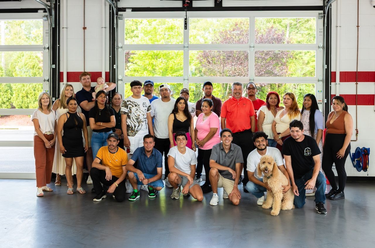 Group of people posing in a bright indoor hall, with large windows and a polished floor.