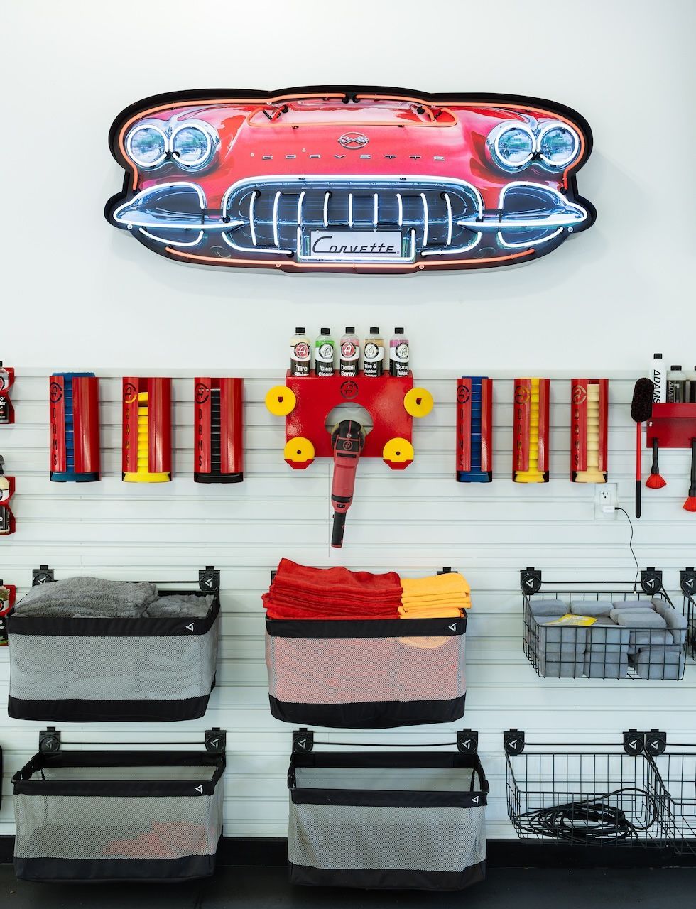 Person in red shirt polishing a green car's hood in a garage, using a power tool.
