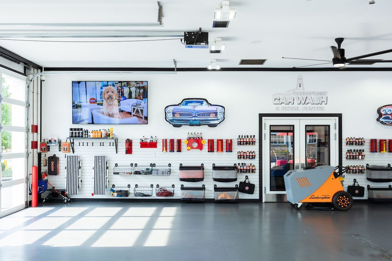 Wide garage interior with automotive tools, wall displays, and an orange forklift near the right wall