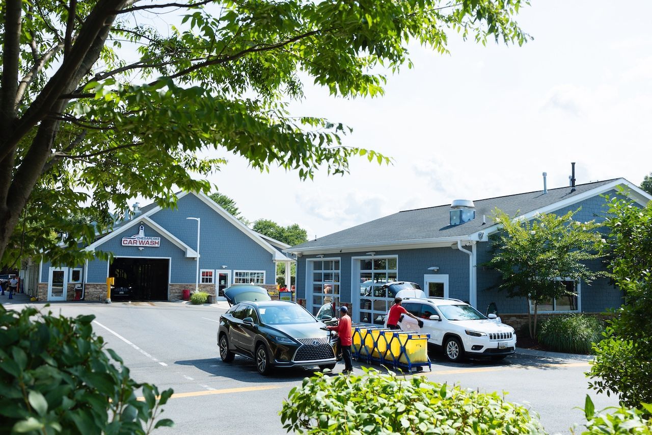 Two parked cars outside a blue building with people and plants in the foreground