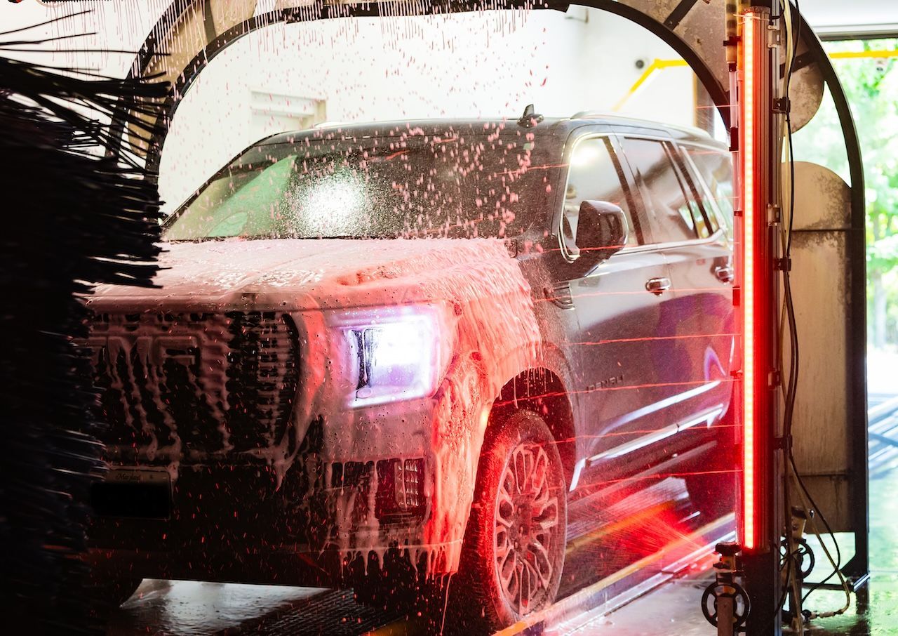 Car being washed in an automatic car wash, covered in soap and lit by red and white lights