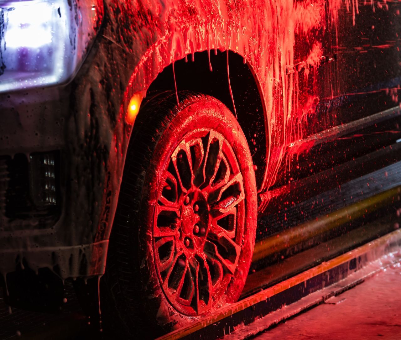Red-lit car wheel splashed with water at a car wash
