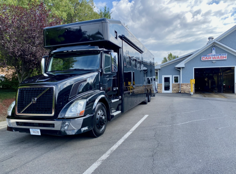 Black Volvo semi-truck with sleeper cab parked outside a garage on a cloudy day.