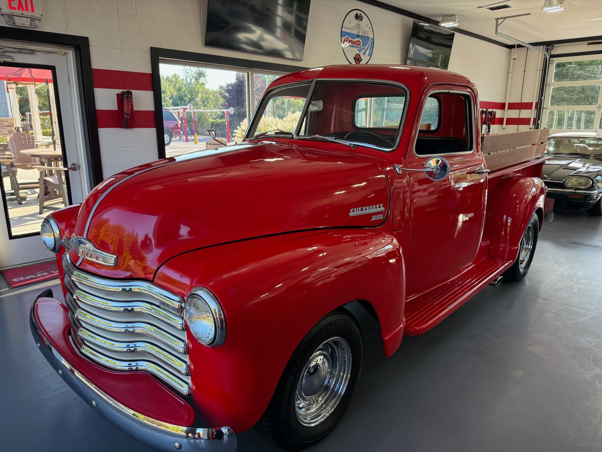 Red vintage pickup truck in a garage, glossy paint and chrome grille.